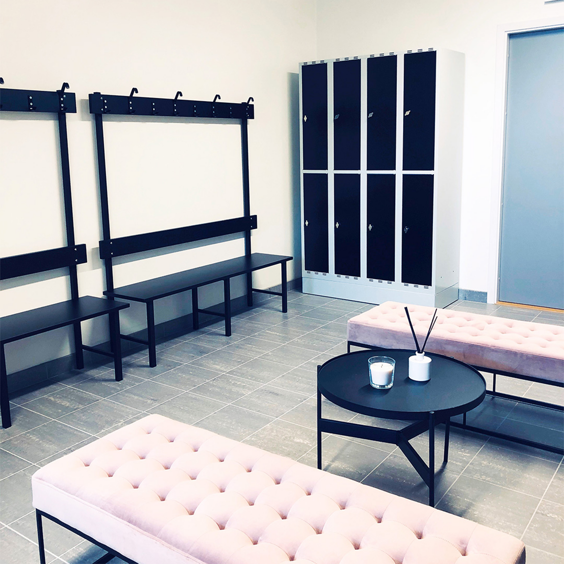 Sittbänk Enkelsektion 1000-2000 mm Svart i omklädningsrum med svart laminat och kroklist för klädförvaring.