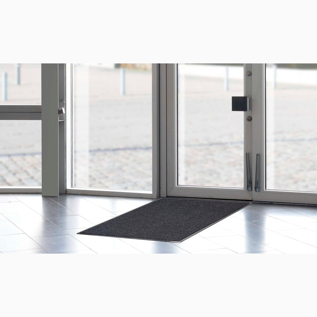 Entrématta Ribb, 900x1500mm i mörk färg placerad vid glasdörr, effektiv för smuts- och vattensamling i entréer.